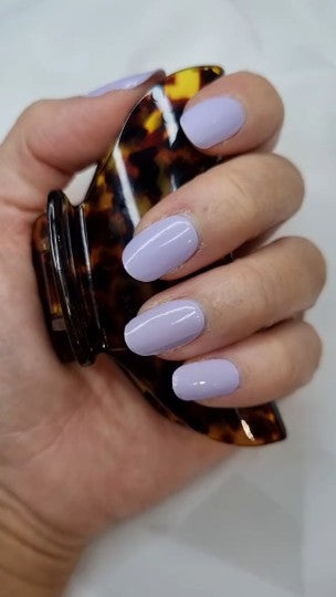 Hand with light purple nail polish holding a tortoiseshell hair clip against a white background